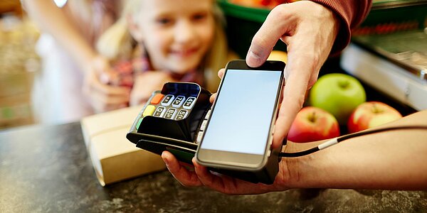 Familie bezahlt in einem Geschäft mittels Smartphone an einem mobilen Kartenlesegerät