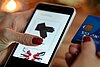 Eine Frau durchsucht auf ihrem Smartphone einen Onlineshop und hält in der anderen Hand ihre Kreditkarte