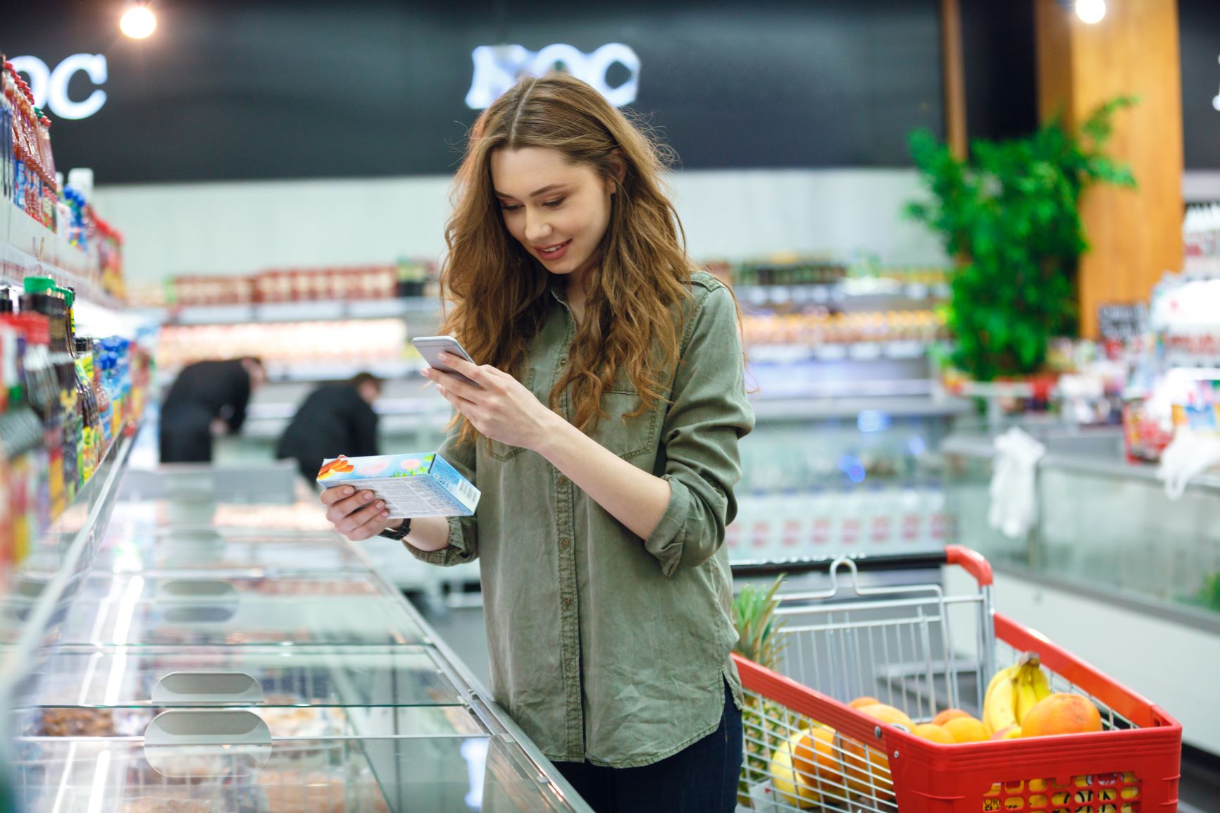 Eine Frau scannt in einem Supermarkt mit ihrem Smartphone ein Produkt aus der Tiefkühltruhe.